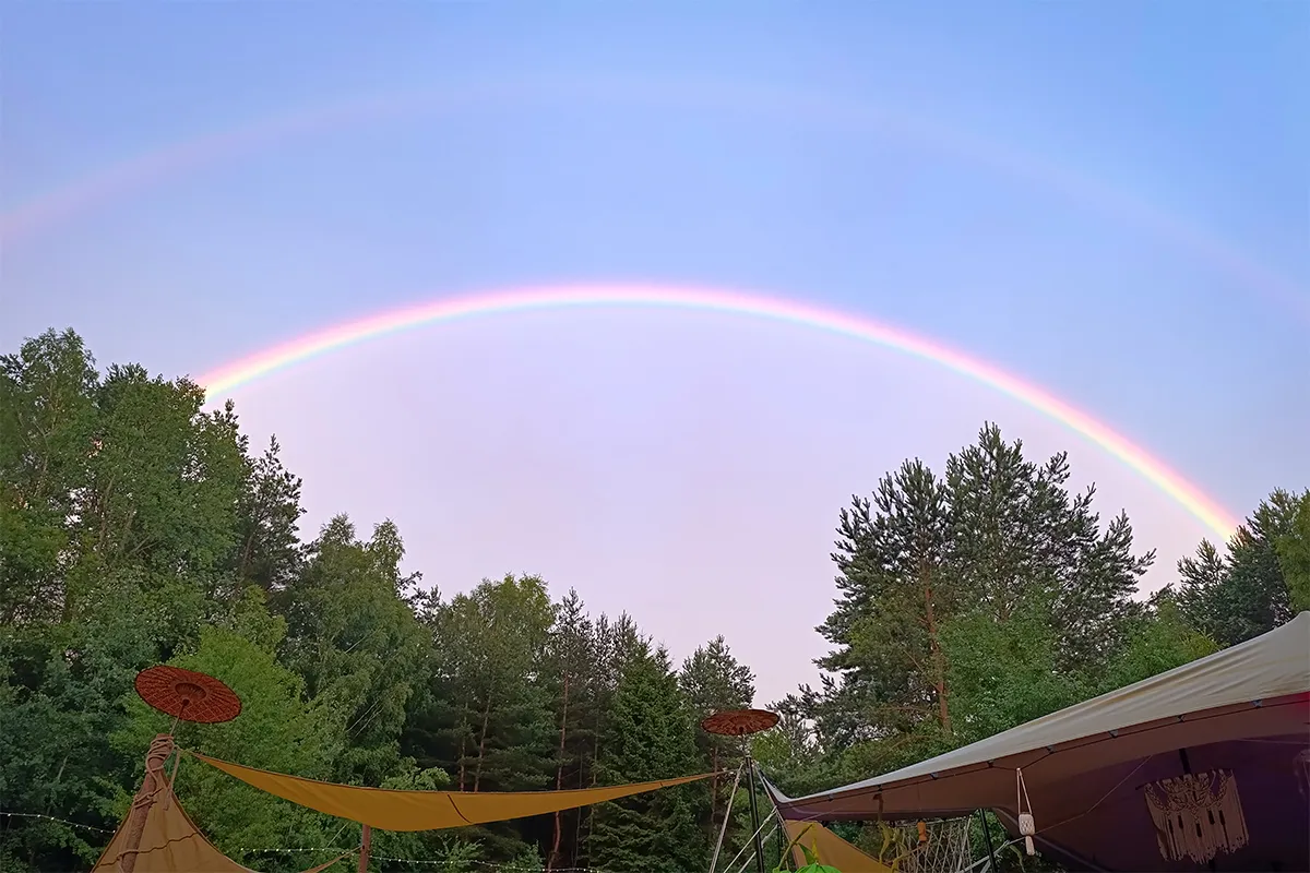 Double rainbow arching above trees and tent canopies